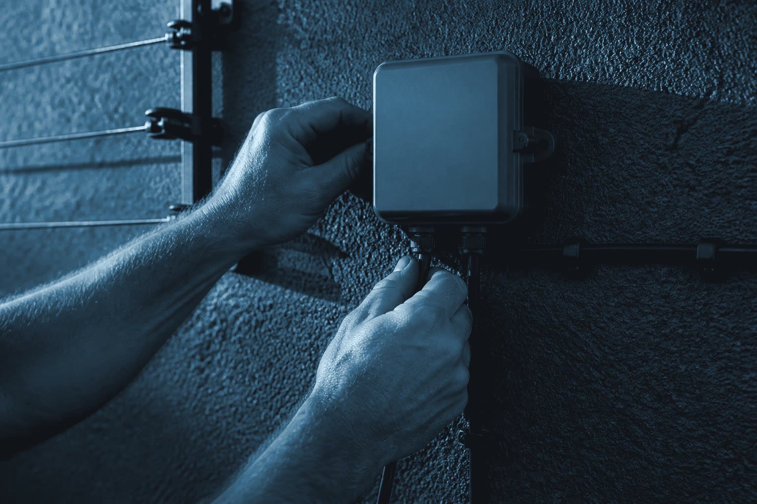 Hands fitting an electric fence energiser box to a boundary wall